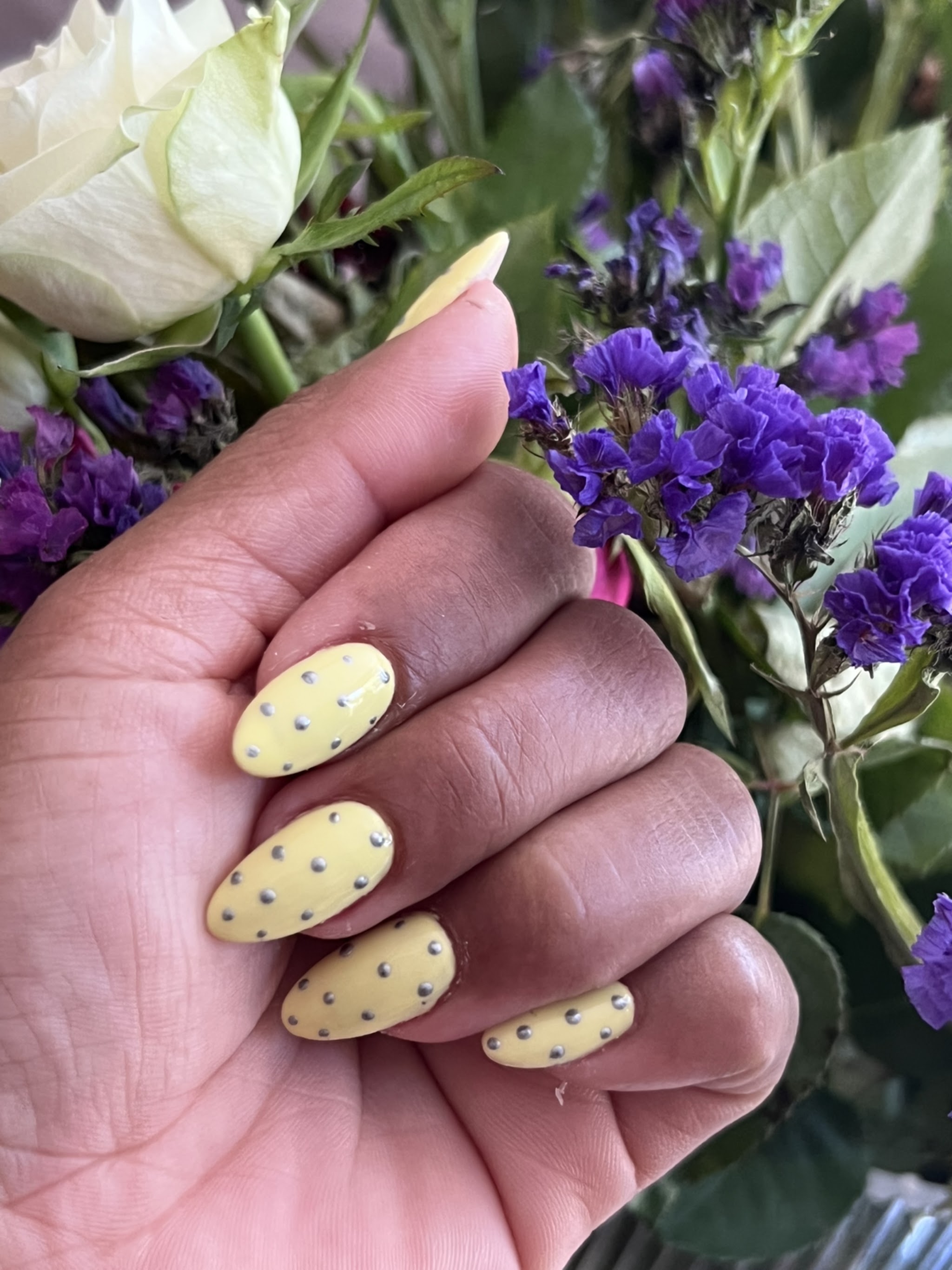 Gele manicure met donkere stipjes naast een boeket bloemen